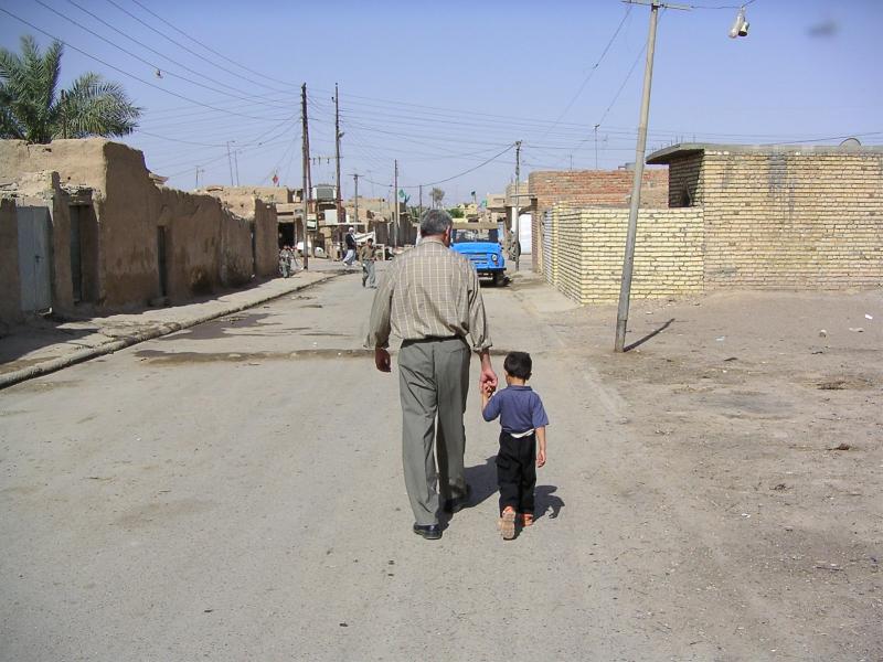 Photograph of a man holding the hand of a child, walking away down a street somewhere in Iraq. Photograph by an American soldier of C Co, 1/252 Army Reserve Battalion. 